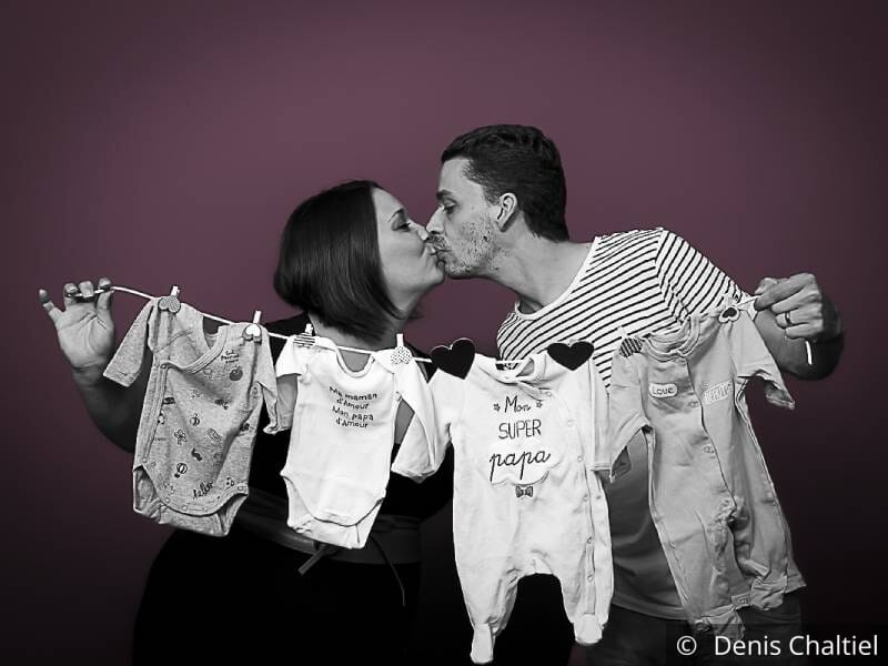 Un couple tient une corde à linge sur laquelle sont pendus des vêtements de bébé.